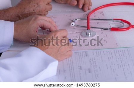 Doctor hands with cardiogram chart with pen. Cardiologist explaining his patient EKG results. World Heart Day concept.