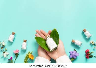 Doctor hands holding homeopathic globules​ bottle with wild flowers​ on green backgound. Homeopathy alternative medicine concept. Flat​ layout. Copy space.