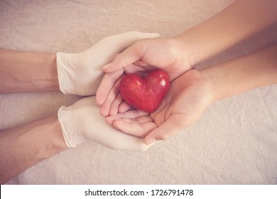 Doctor hands with medical gloves holding child hands and red heart, health insurance,organ donation, charity during covid-19 coronavirus pandemic, saving life, thank you and appreciation to doctor