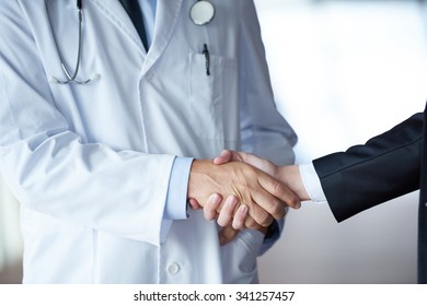 Handschüttelei mit einem Patienten bei Ärzten in einem modernen, hellen Krankenhaus