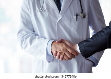 Handschüttelei mit einem Patienten bei Ärzten in einem modernen, hellen Krankenhaus-Büro
