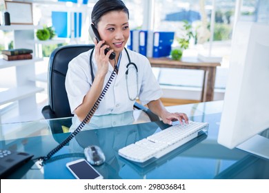 Doctor Having Phone Call And Using Her Computer In Medical Office