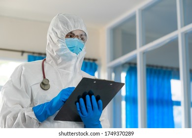 Doctor In Hazmat PPE Protective Clothing Wearing Protective Mask To Protect Against Covid-19 Are Check Patient Information In Hospital.