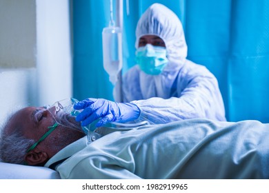 Doctor Hazmat Or Protective Suit Helping To Wear Ventilation Oxygen Mask To Covid Infected Difficulty In Breathing To Patient At Hospital - Concept Of Dyspnea Due To Coronavirus Lung Infection