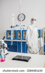 Doctor In Hazmat Suit Holding Sprayer While Looking At Camera In Lab