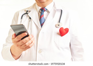 Doctor With A Heart On The Lapel Consulting The Cell Phone To View Patient Data. Health And Care Concept