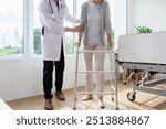 Doctor help old elderly caucasian woman uses walker and walking for physical therapy or unhealthy injury woman patient walking via four legs walker. Savings and senior health insurance concept 