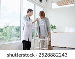 Doctor help old elderly caucasian woman uses walker and walking for physical therapy or unhealthy injury woman patient walking via four legs walker. Savings and senior health insurance concept 