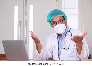 A Doctor In His Mask And Hair Net Sitting In Front Of Laptop Giving Virtual Advise To His Patient Through Internet Connection To Reduce Physical Interaction During Corona Pandemic