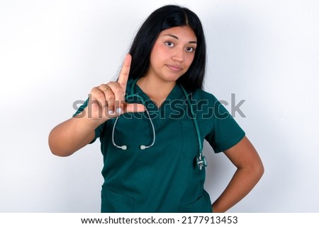 Doctor hispanic woman wearing surgeon uniform over white background making fun of people with fingers on forehead doing loser gesture mocking and insulting.