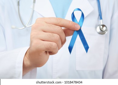 Doctor holding blue ribbon, closeup. Cancer awareness concept