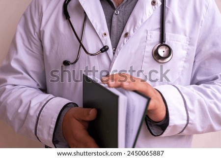 A doctor is holding a book in his hand. The book is green and white
