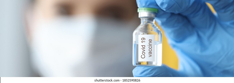 Doctor holding bottle with covid-19 vaccine in rubber glove in his hand in laboratory close-up. Coronavirus vaccination study concept.