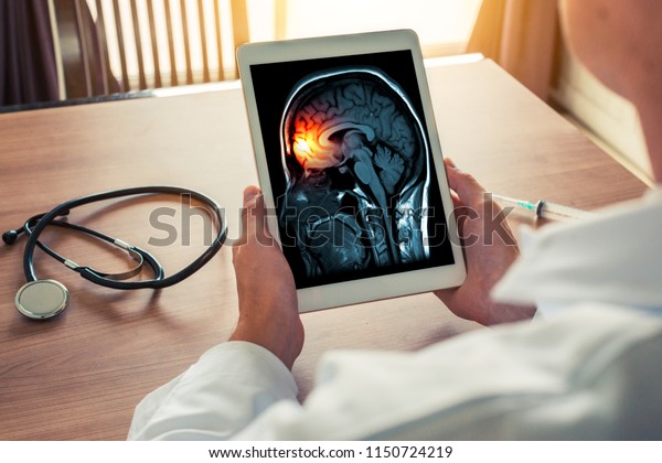 Doctor holding a digital tablet with\
x-ray of brain and skull skeleton. Headache, meningitis and\
migraine concept with stethoscope and syringe on the\
desk