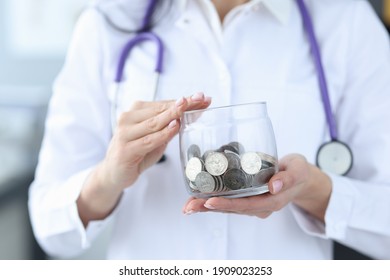 Doctor holding glass jar with coins closeup. Paid medicine concept