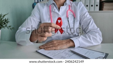 Doctor holding in his hands red ribbon symbol of fight against HIV and AIDS closeup. Stop hiv aids concept