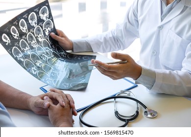 Doctor Holding And Looking At X-ray Film Examining At Brain By Ct Scan Of Patient And Analyze Result While Discussing Explaining Problem Of Medical.