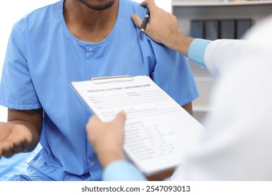 Doctor holding medical form having discussion with patient in hospital room. Patient and a surgeon discuss a condition in a hospital, wearing scrubs and consulting in a clinic room. - Powered by Shutterstock