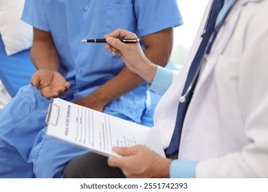 Doctor holding medical form having discussion with patient in hospital room. Patient and a surgeon discuss a condition in a hospital, wearing scrubs and consulting in a clinic room. - Powered by Shutterstock