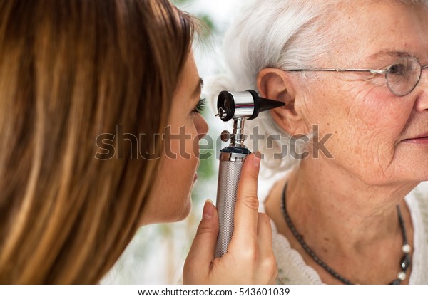 Doctor holding otoscope and examining ear of\
senior woman in\
ambulance
