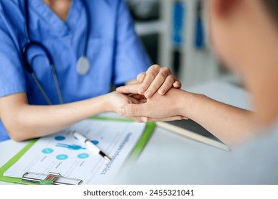 A doctor is holding a patient's hand while they are in a hospital room. The patient is wearing a blue shirt and the doctor is wearing a blue scrubs - Powered by Shutterstock