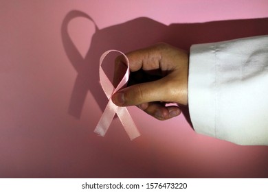 Doctor Holding A Pink Ribbon On A Pink And White Background. Ribbon In Tribute To Breast Cancer Patients.