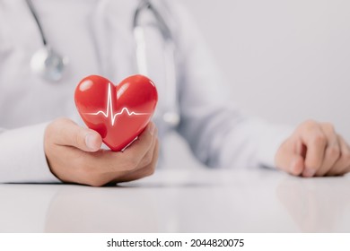 The doctor is holding and showing a red heart with life graph on white background.
