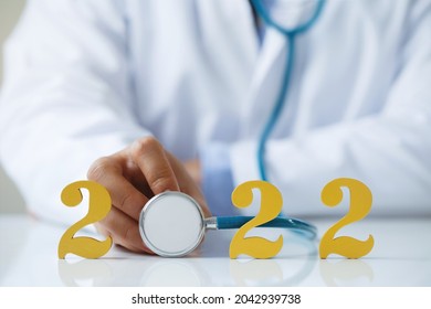 Doctor holding stethoscope near gold wooden number 2022 on desk. Idea for new trend in medicine treatment and diagnosis.Happy New Year for healthcare and medical concepts.