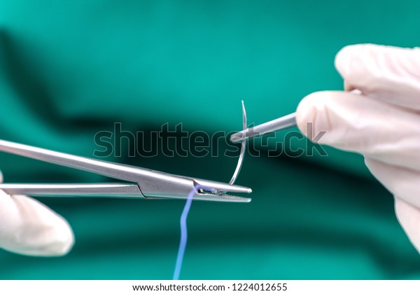 Doctor holding surgical forceps suture needle,\
suturing material