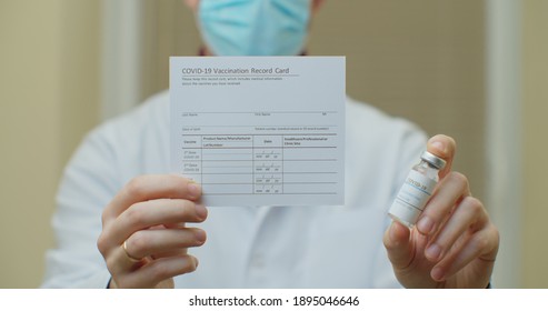 Doctor Is Holding A Vaccination Record Card And Corona Virus Vaccine Vials. Passport Of Immunity To The Coronavirus In The Hands Of A Male Doctor. Health Passport As Proof Of Recovery From COVID-19.