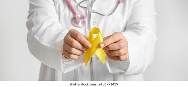 Doctor holding yellow ribbon on light background, closeup. Banner for Sarcoma Cancer Awareness Month - Powered by Shutterstock