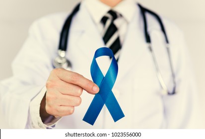 Doctor Holds Blue Ribbon,  Colon Cencer Awareness. Symbolic Concept Raising Awareness Concerns Help Campaign On People Living Colorectal Cancer Illness.