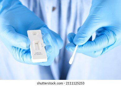The doctor holds a COVID-19 swab collection, wears blue gloves and a PPE protective mask, and carries a test tube to collect the OP NP and test coronavirus.