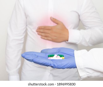 The doctor holds pills in his hand against the background of a man who holds on to the stomach for pain and inflammation in the stomach. The concept of drug treatment of gastritis and stomach ulcers - Shutterstock ID 1896995830