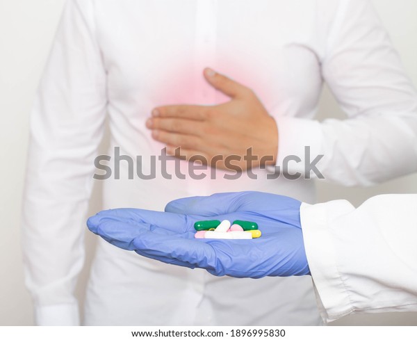 The doctor holds pills in his hand against the\
background of a man who holds on to the stomach for pain and\
inflammation in the stomach. The concept of drug treatment of\
gastritis and stomach\
ulcers