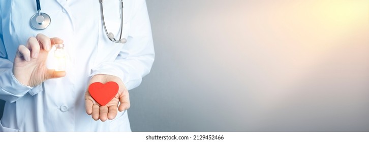 The doctor holds a red heart in one hand and an ampoule with a transparent liquid in the other (medicine, vaccine). Medical background with copy space and sunbeams. The concept of health, treatment,  - Powered by Shutterstock - Get 15% off with code: PIKWIZARD15
