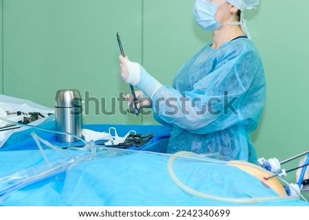 The doctor holds a sterile surgical instrument near the table in the operating room.