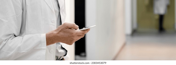 Doctor in hospital looking at mobile phone - Shutterstock ID 2303453079
