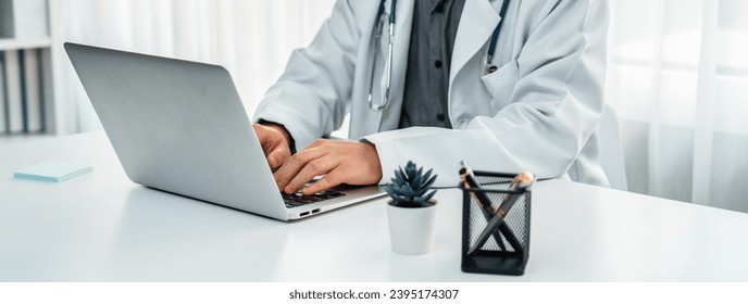 Doctor at hospital sit at his desk working on laptop diagnosing patient test results, developing treatment plan for illnesses and sicknesses. Medical staff and healthcare service. Panorama Rigid - Shutterstock ID 2395174307