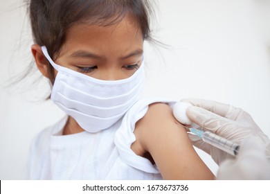 Doctor Injecting Vaccination On Asian Child Girl Arm. The Child Girl Wearing Protection Mask For Protect Air Smog Pollution With PM 2.5 And Covid-19 Virus. Healthy And Medical Concept.