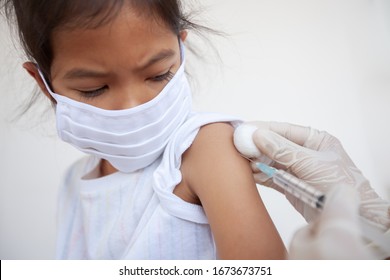 Doctor Injecting Vaccination On Asian Child Girl Arm. The Child Girl Wearing Protection Mask For Protect Air Smog Pollution With PM 2.5 And Covid-19 Virus. Healthy And Medical Concept.