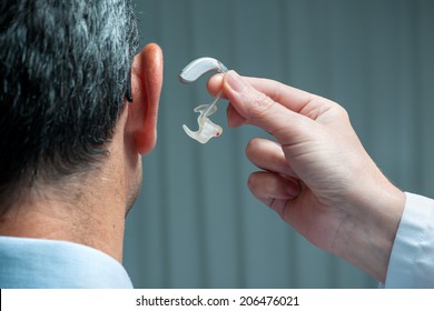 Doctor Inserting Hearing Aid In Senior's Ear