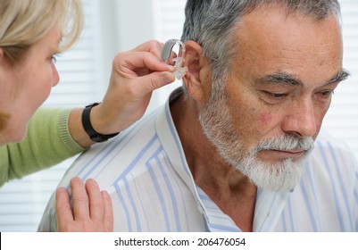 Doctor Inserting Hearing Aid In Senior's Ear