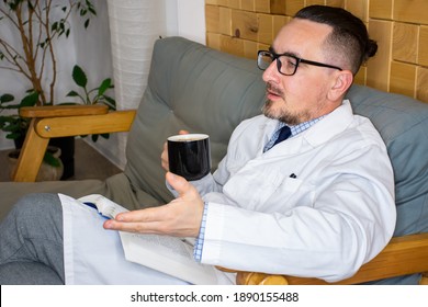 Doctor Of Internal Medicine Or General Practitioner Relaxing On Couch With Cup Of Coffee Or Tea And Talking With Colleagues Or Examining Patient In His Office. Concept Photo Of Doctor Hospital Resting