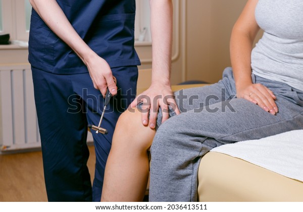 Doctor knocks a hammer on the knee\
of a girl, checking reflexes at a doctor\'s\
appointment