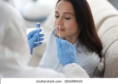 Médico assistente de laboratório em traje de proteção tira cotonete do nariz do paciente doente em casa. Testes laboratoriais para o conceito de coronavírus.