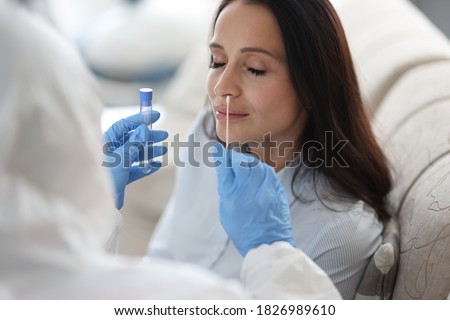 Doctor laboratory assistant in protective suit takes swab from nose of sick patient at home. Laboratory tests for coronavirus concept.
