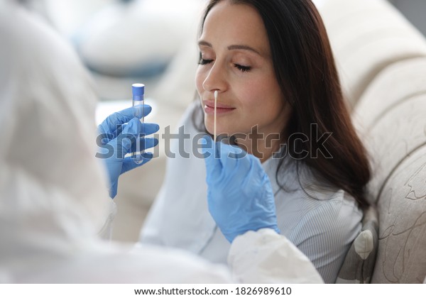 Doctor laboratory assistant in protective suit\
takes swab from nose of sick patient at home. Laboratory tests for\
coronavirus concept.
