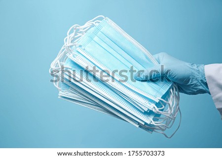 Doctor in latex gloves holding disposable face masks on light blue background, closeup. Protective measures during coronavirus quarantine