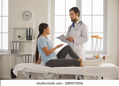 Doctor Listening To Female Patient With Limb Injury. Young Woman With Broken Leg Talking To Orthopedic Surgeon, Traumatologist Or Physiatrist During Medical Exam In Office Of Hospital Or Clinic